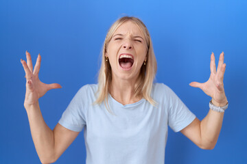 Young caucasian woman wearing casual blue t shirt crazy and mad shouting and yelling with aggressive expression and arms raised. frustration concept.