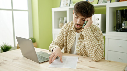 Young arab man talking on smartphone reading document at home