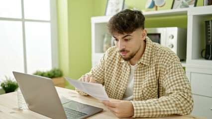 Fototapeta na wymiar Young arab man using laptop reading document at home