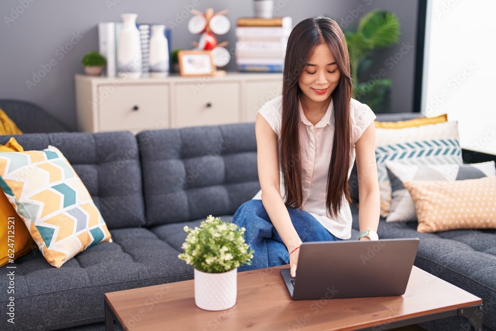 Canvas Prints Young chinese woman using laptop sitting on sofa at home