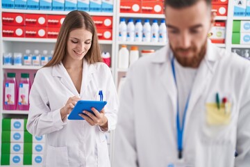 Man and woman pharmacists using touchpad working at pharmacy