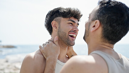 Two men couple smiling confident touching face at seaside