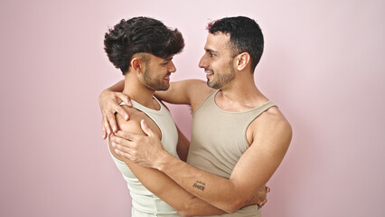Two men couple smiling confident hugging each other over isolated pink background