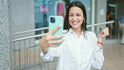 Plakat Young beautiful hispanic woman smiling confident having video call at street