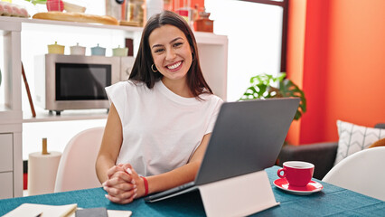 Young beautiful hispanic woman smiling confident using laptop at dinning room