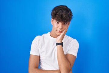 Hispanic teenager standing over blue background thinking looking tired and bored with depression problems with crossed arms.