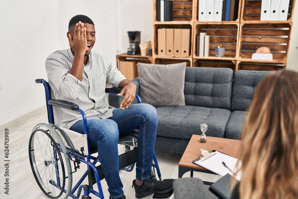 Wall mural african american man doing therapy sitting on wheelchair covering one eye with hand, confident smile