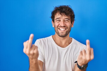 Hispanic young man standing over blue background showing middle finger doing fuck you bad expression, provocation and rude attitude. screaming excited