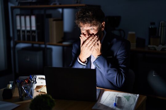Hispanic young man working at the office at night shocked covering mouth with hands for mistake. secret concept.