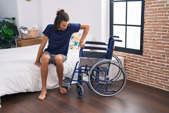 Young hispanic man disabled trying to sit on wheelchair at bedroom