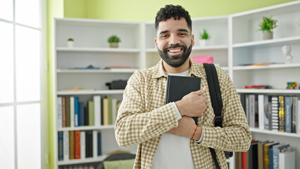 Young hispanic man student smiling confident holding book at library university