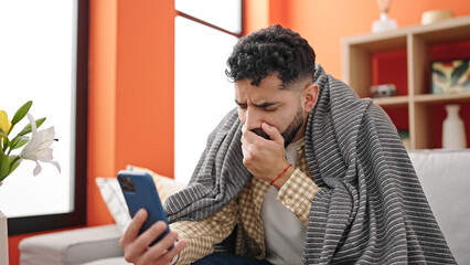 Young hispanic man sitting on sofa having online medical consultation coughing at h