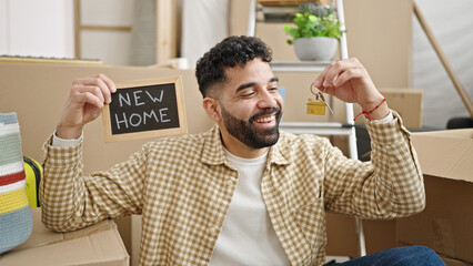 Fototapeta premium Young hispanic man smiling confident holding blackboard and keys at new home