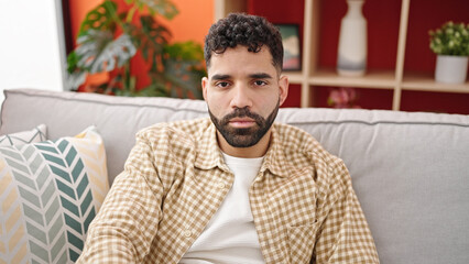 Young hispanic man sitting on sofa with relaxed expression at h