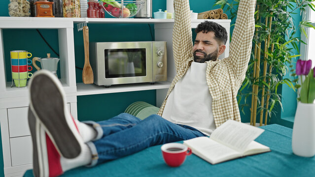 Young hispanic man sitting on table stretching arms at dinning room