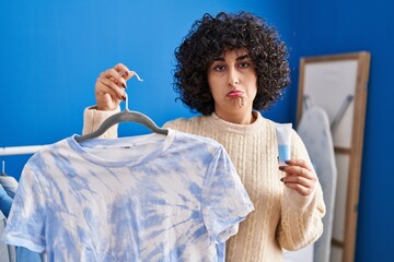 Young brunette woman with curly hair dyeing tye die t shirt depressed and worry for distress,...