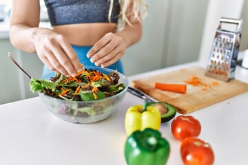 Young woman pouring carrot on salad at kitchen