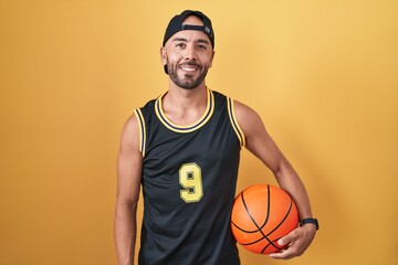 Middle age bald man holding basketball ball over yellow background with a happy and cool smile on face. lucky person.