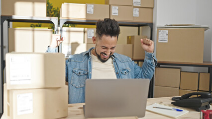 Young latin man ecommerce business worker using laptop with winner expression at office