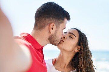 Young hispanic couple make selfie by the camera kissing at seaside