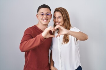 Mother and son standing together over isolated background smiling in love doing heart symbol shape with hands. romantic concept.