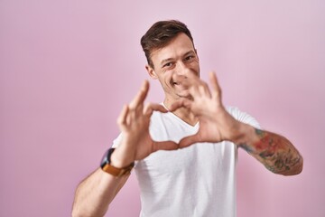 Caucasian man standing over pink background smiling in love doing heart symbol shape with hands. romantic concept.