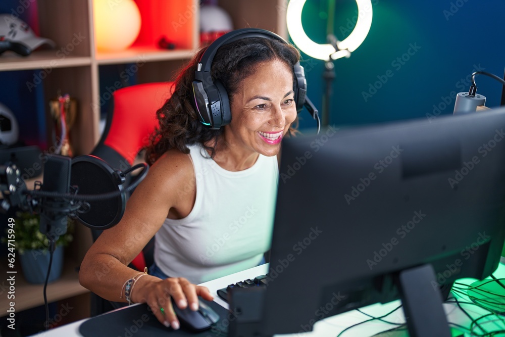 Wall mural Middle age woman streamer playing video game using computer at gaming room