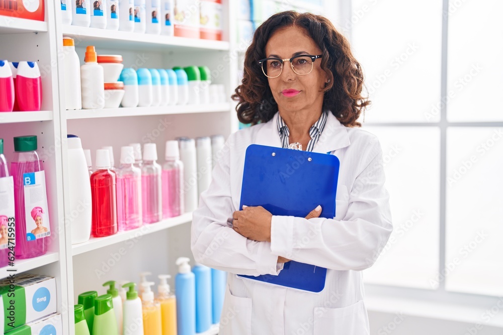 Wall mural middle age woman pharmacist holding clipboard at pharmacy