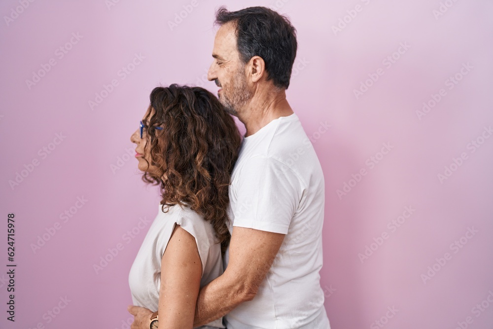 Poster Middle age hispanic couple together over pink background looking to side, relax profile pose with natural face and confident smile.