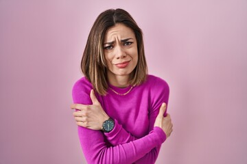 Hispanic woman standing over pink background shaking and freezing for winter cold with sad and shock expression on face