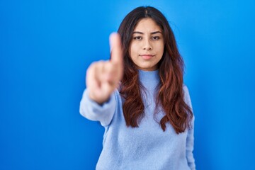 Fototapeta premium Hispanic young woman standing over blue background pointing with finger up and angry expression, showing no gesture