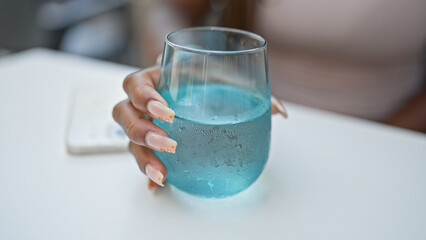 African american woman holding glass of water sitting on table at coffee shop terrace