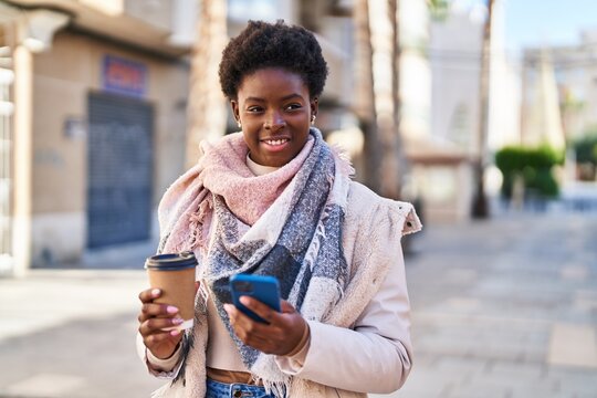 African american woman using smartphone drinking coffee at street