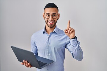 Young hispanic man working using computer laptop pointing finger up with successful idea. exited...
