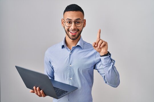 Young hispanic man working using computer laptop pointing finger up with successful idea. exited and happy. number one.