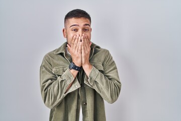 Young hispanic man standing over isolated background laughing and embarrassed giggle covering mouth...