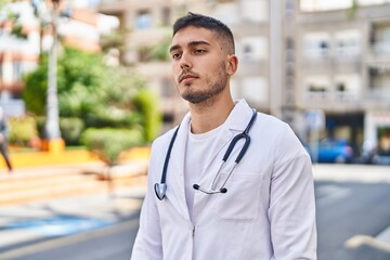 Young hispanic man doctor standing with relaxed expression at park