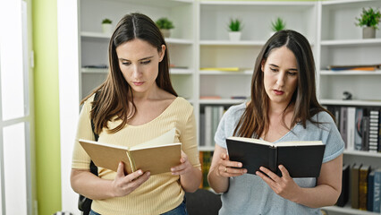 Two women standing reading books at library university