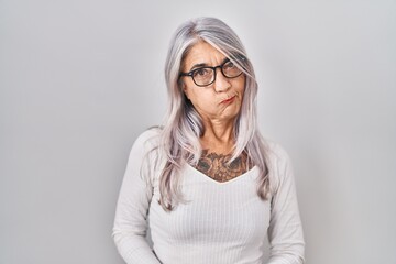 Middle age woman with grey hair standing over white background puffing cheeks with funny face. mouth inflated with air, crazy expression. - obrazy, fototapety, plakaty