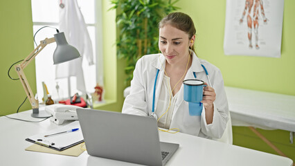 Young beautiful hispanic woman doctor listening to music drinking coffee at clinic