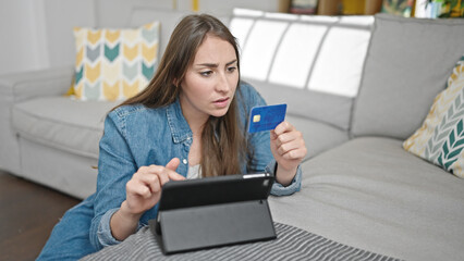 Young beautiful hispanic woman shopping with touchpad and credit card looking upset at home