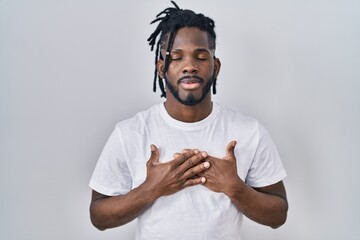 African man with dreadlocks wearing casual t shirt over white background smiling with hands on chest with closed eyes and grateful gesture on face. health concept.