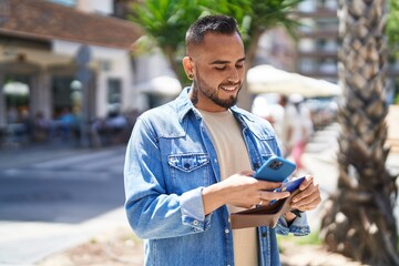 Young hispanic man using smartphone and credit card at street