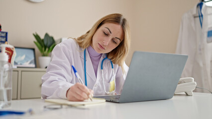 Young beautiful hispanic woman doctor using laptop taking notes at clinic