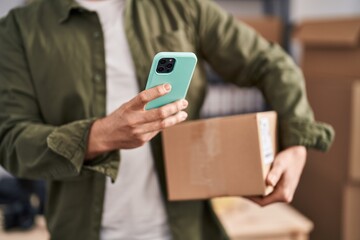 Young caucasian man ecommerce business worker using smartphone holding package at office