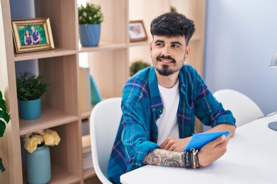 Young hispanic man using touchpad sitting on table at home