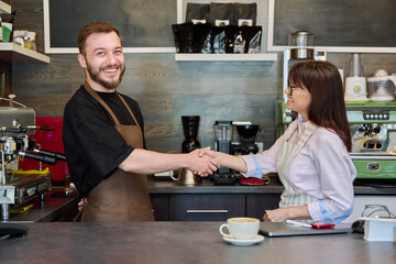 Colleagues, partners, man and woman shake hands, in coffee shop