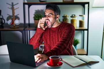 Young hispanic man with beard using computer laptop at night at home shouting and screaming loud to side with hand on mouth. communication concept.