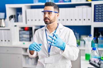 Young hispanic man scientist speaking at laboratory