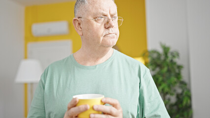 Middle age grey-haired man drinking coffee standing at home